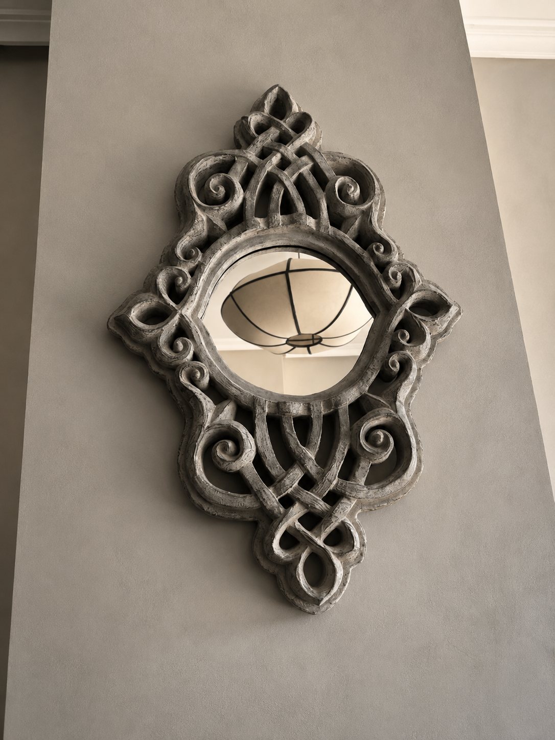 Ornate carved mirror on a soft grey wall reflecting the living room pendant