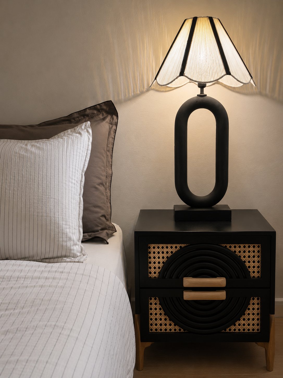 Sculptural black bedside lamp on a cane-front cabinet beside striped bedding