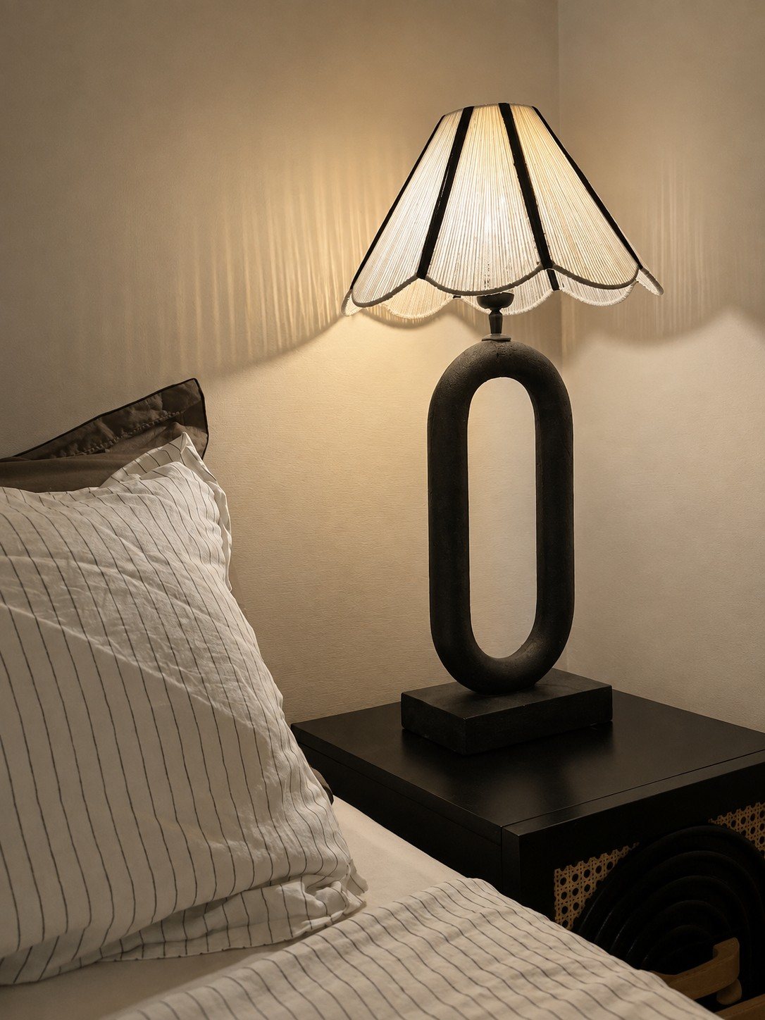 Bedside lamp with a scalloped shade beside layered pillows