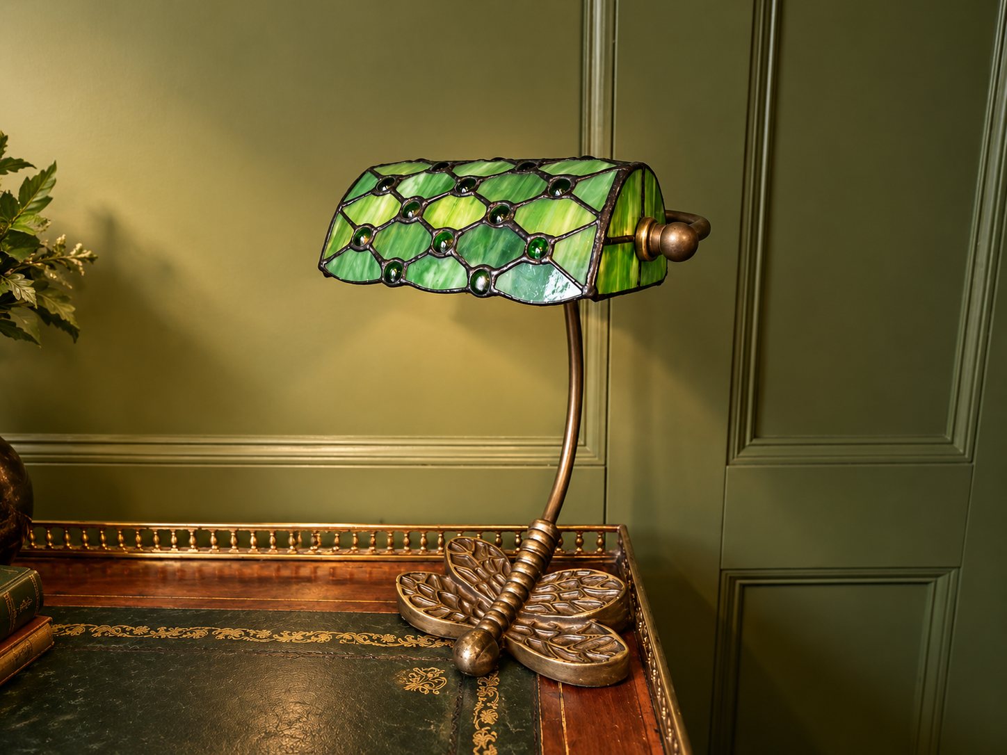 Green Tiffany-style lamp on a leather-topped desk against green panelling