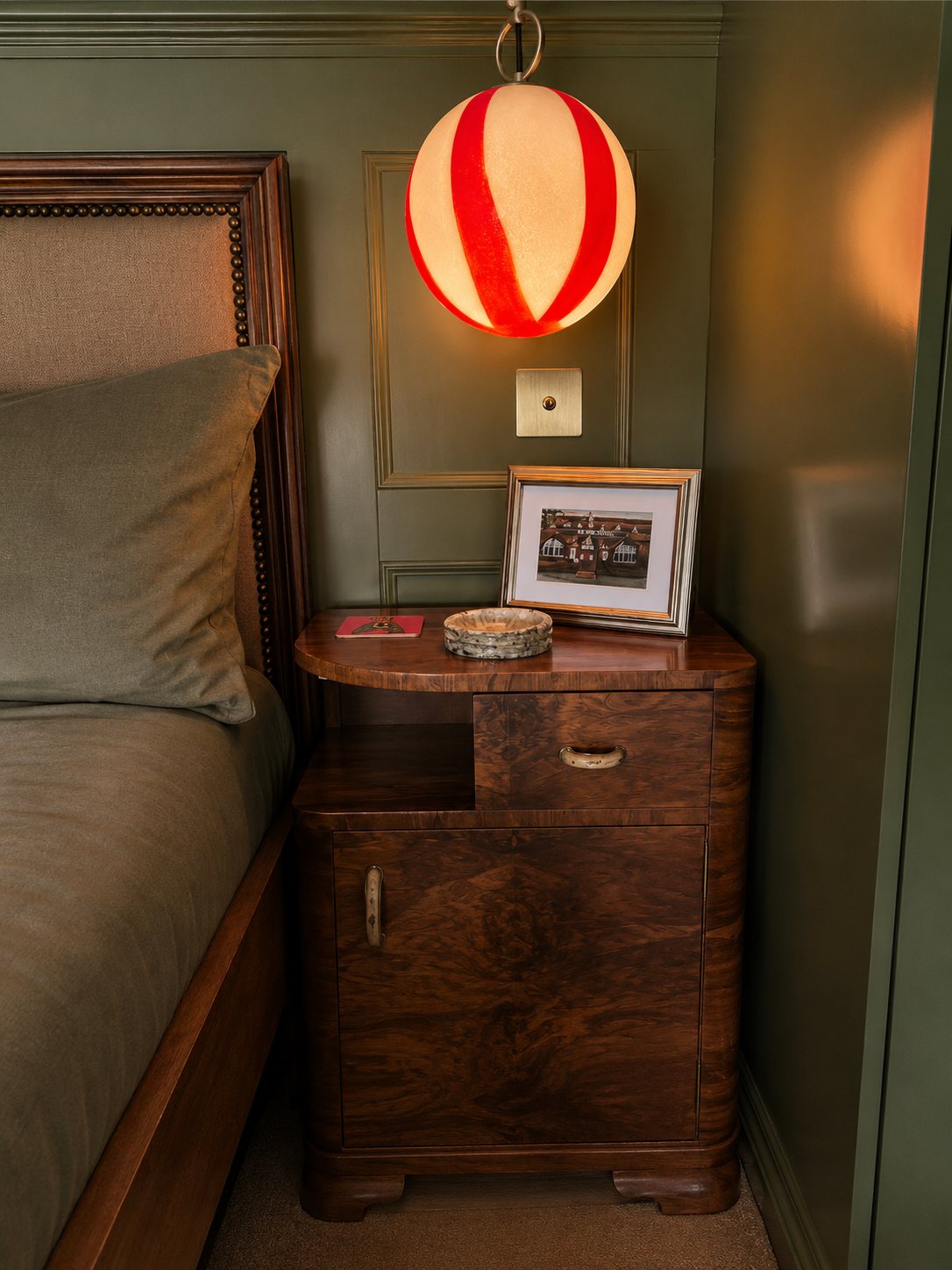 Burr walnut bedside cabinet beneath a striped glass pendant against green panelling